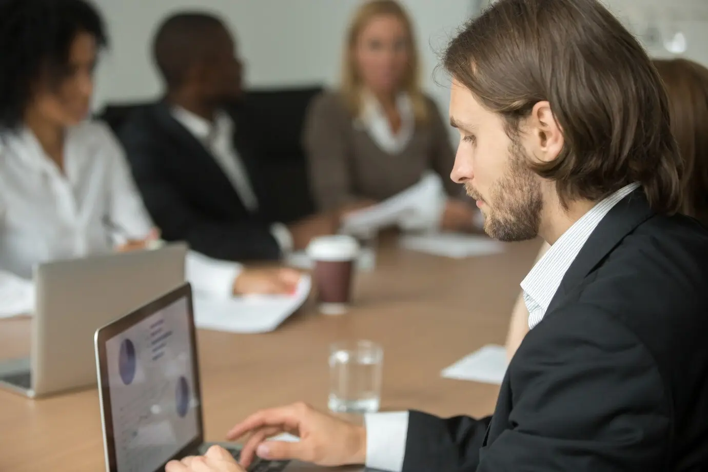 Serious businessman using a laptop to work online during a meeting with a diverse group.